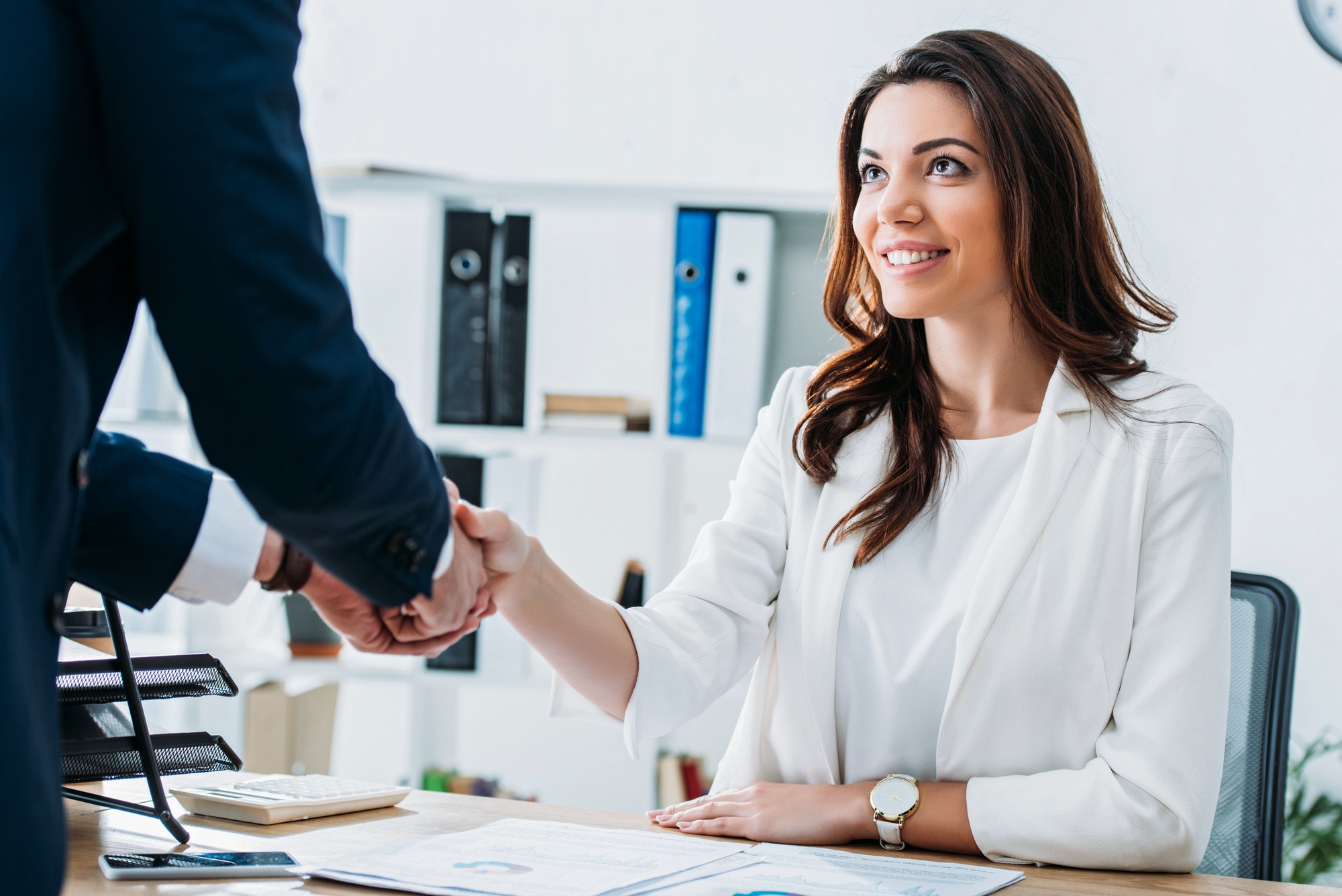 beautiful and smiling advisor and investor in suits shaking hands at workplace
