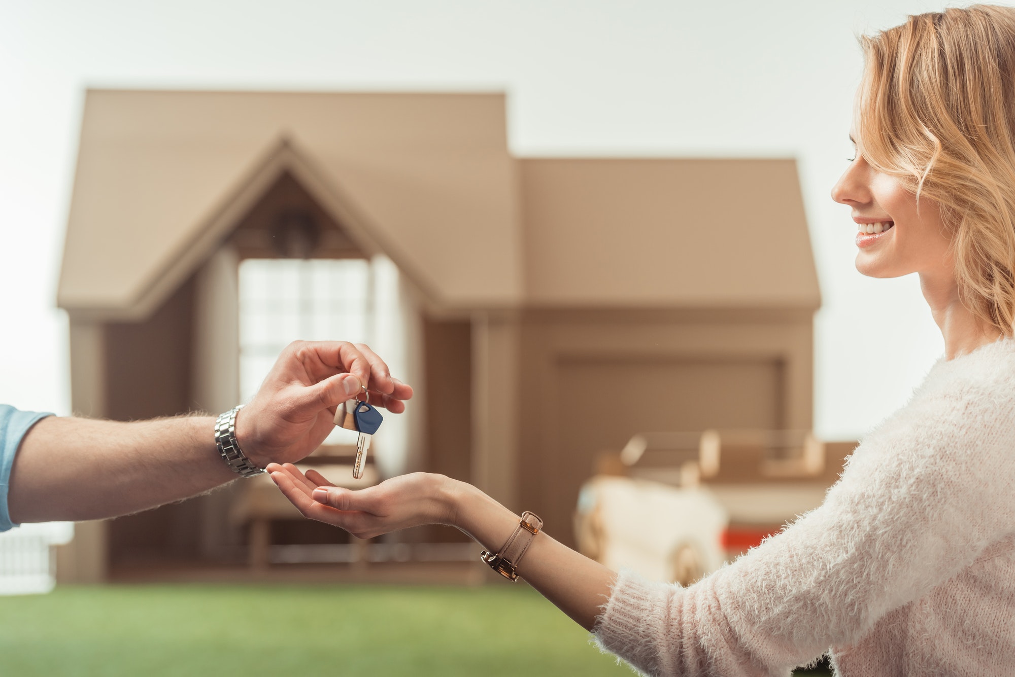 cropped shot of real estate agent passing key to happy woman in front of cardboard house