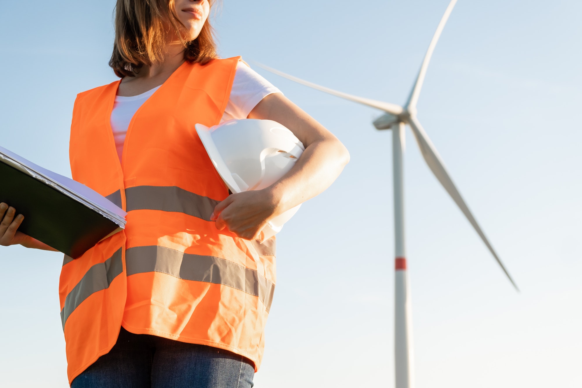 Woman in the orange vest and helmet in the hand holds documents on maintenance of wind turbines on