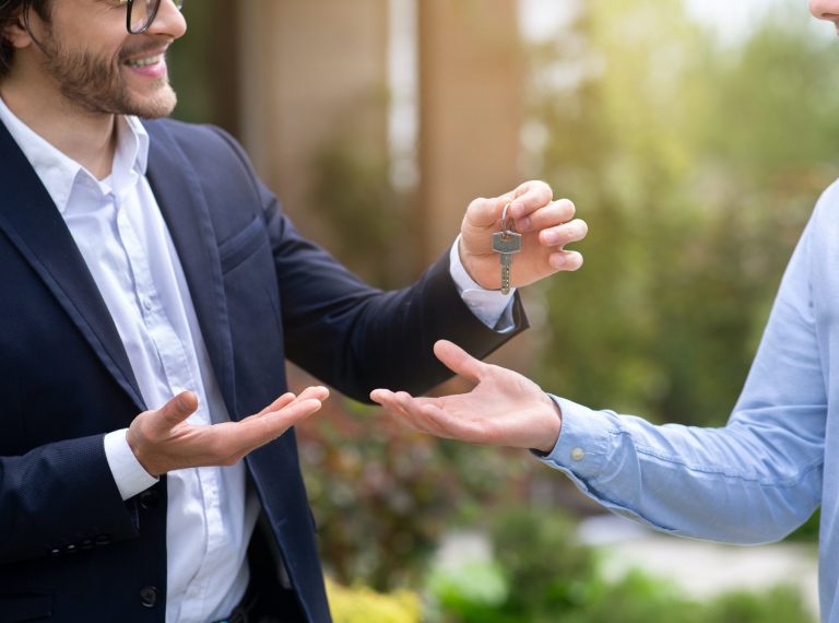 Cropped view of real estate agent giving house key to new home owner near his property, close up