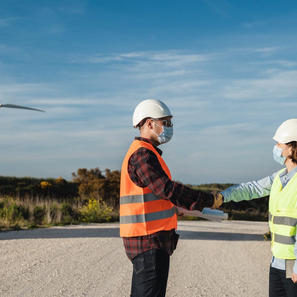Engineer workers discussing projects at wind alternative energy farm wearing safety masks